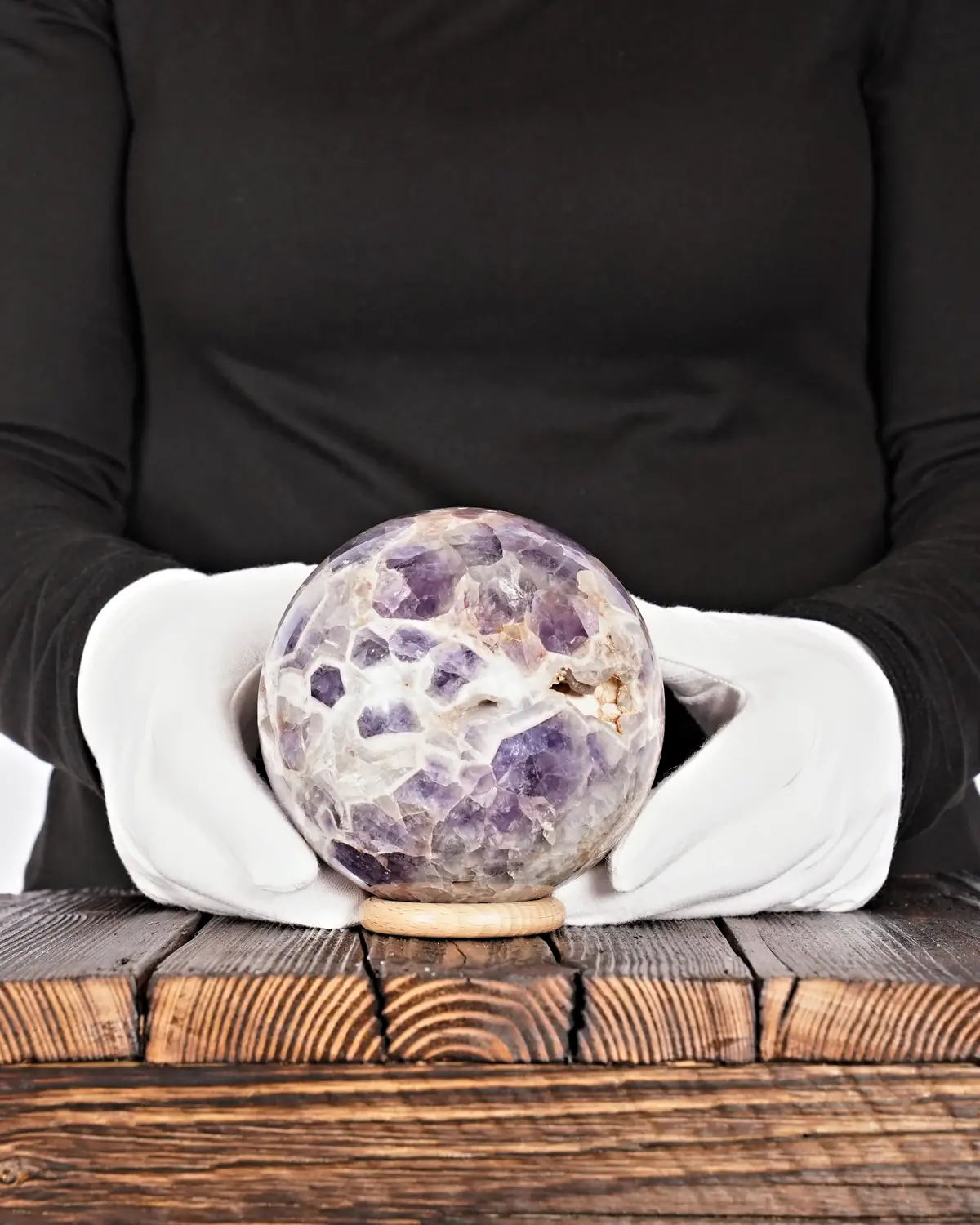 Die Pfote in der Chevron-Amethyst-Kugel in weiss behandschuhten Händen