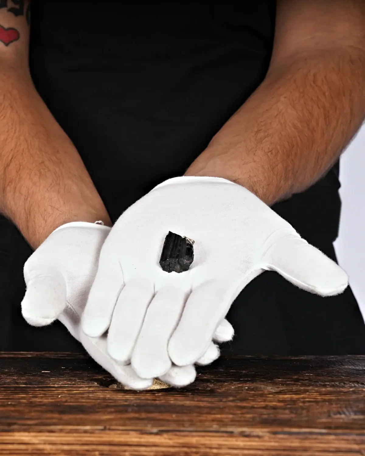 Die kleinen Turmalin-Schörl-Anhänger in weiss behandschuhten Händen