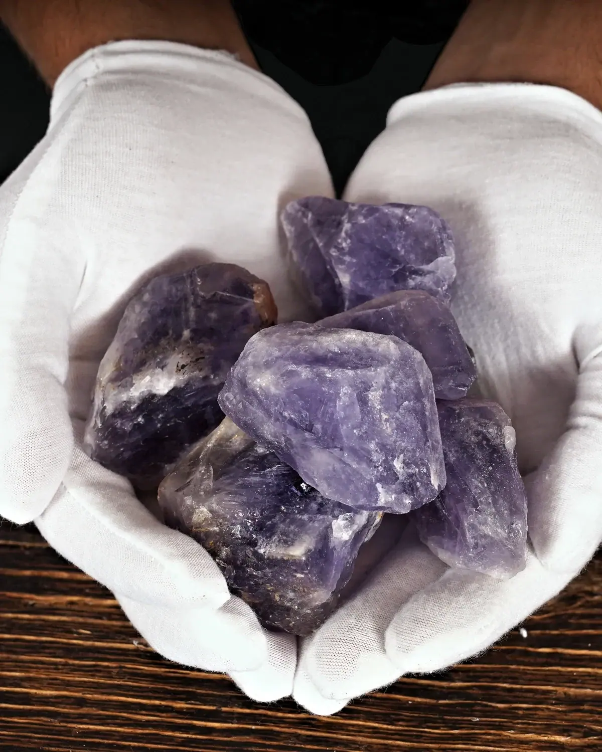 Amethyst-Rohsteine und Wassersteine in weiss behandschuhten Händen