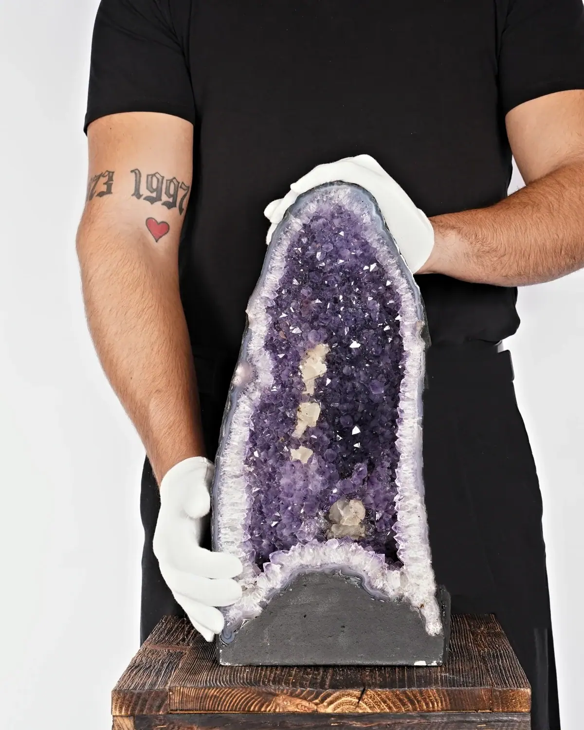 Die leuchtende Amethyst-Druse mit der Calcit-Familie in weiss behandschuhten Händen