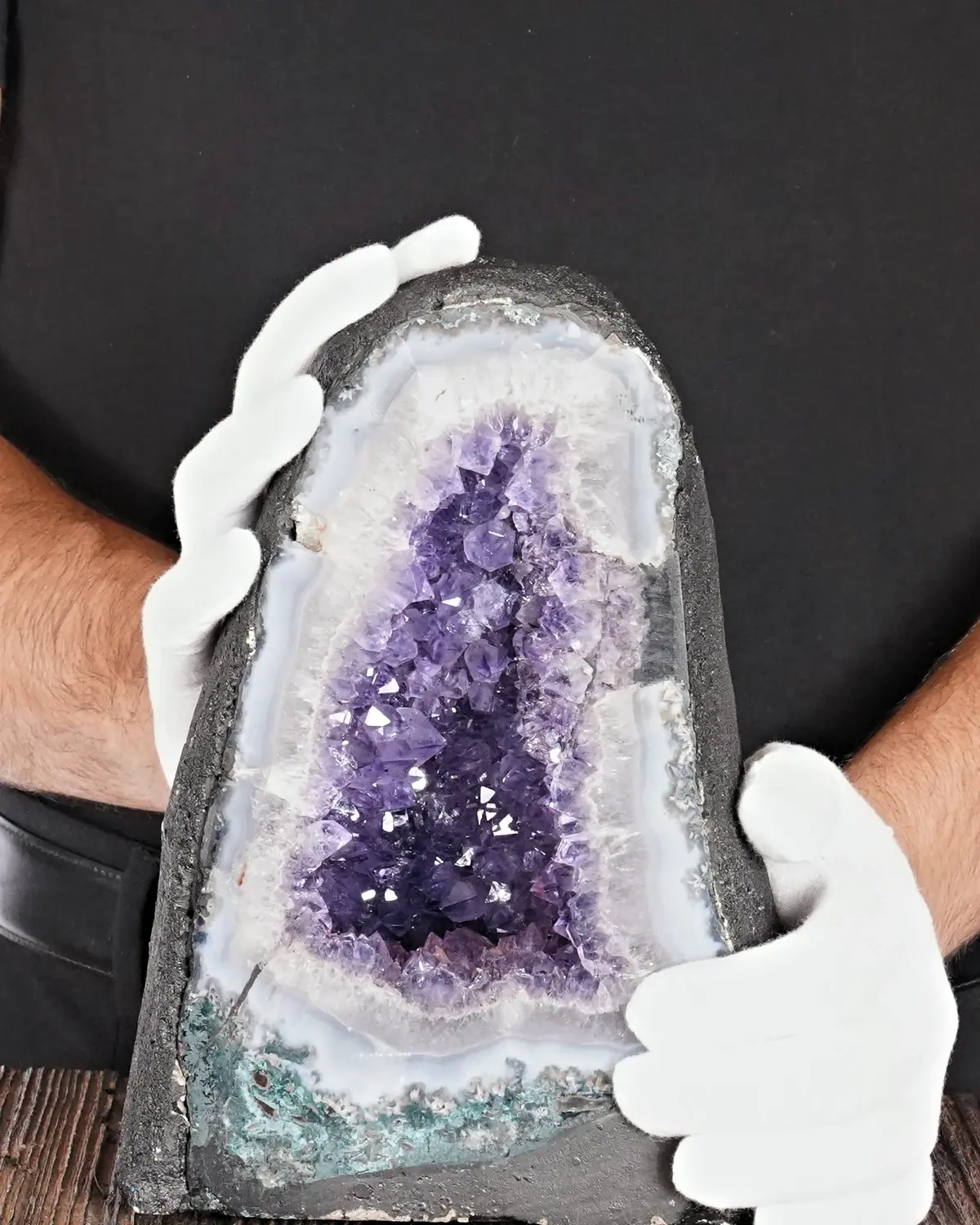 Die lila Amethyst-Höhle mit Goldstaub in weiss behandschuhten Händen
