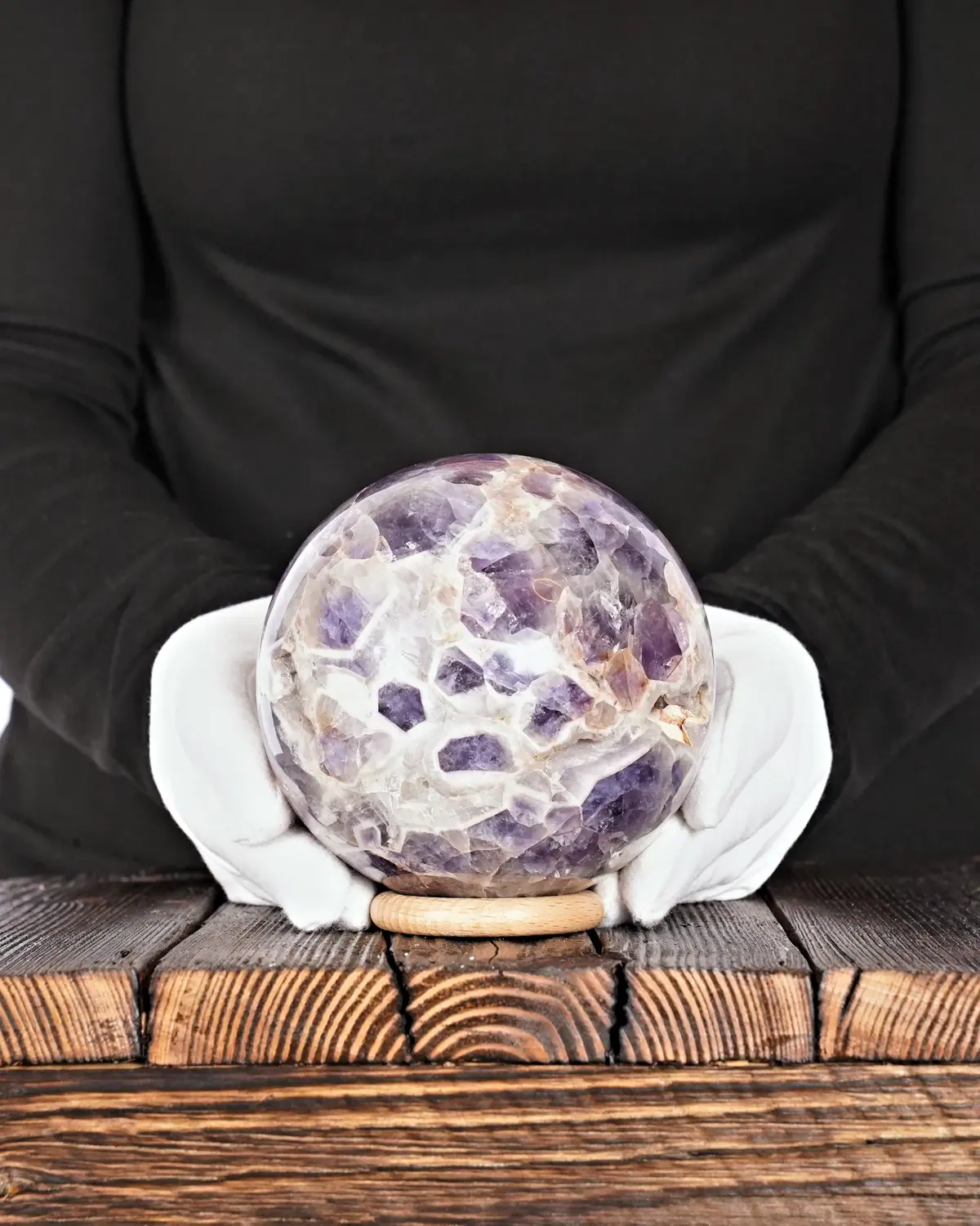 Die Pfote in der Chevron-Amethyst-Kugel in weiss behandschuhten Händen