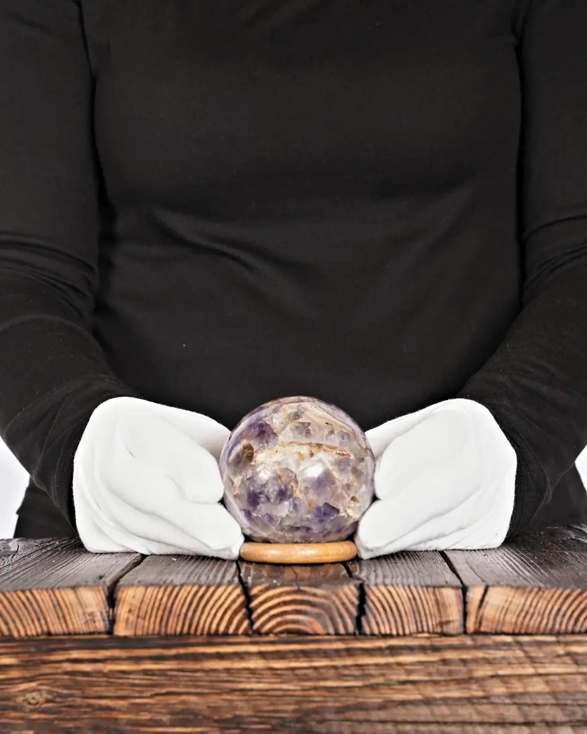 Die antike Chevron-Amethyst-Kugel in weiss behandschuhten Händen