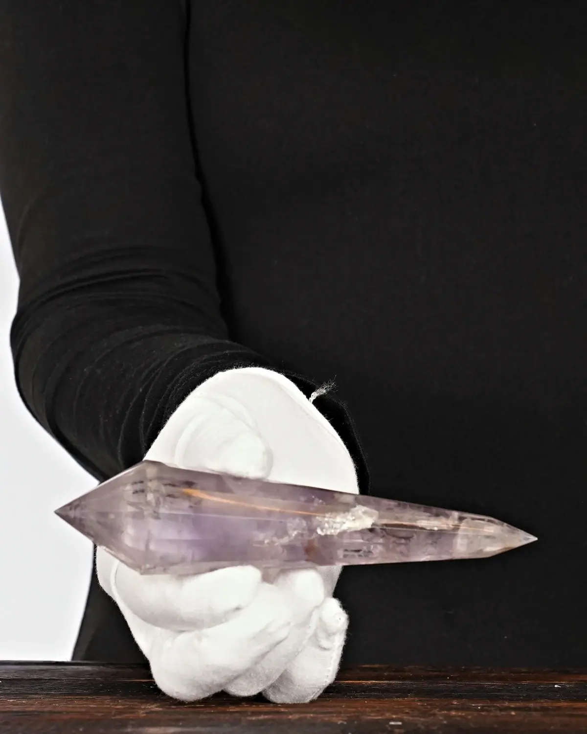 Der 12-fach facettierte, klare Amethyst-Doppelender in weiss behandschuhten Händen