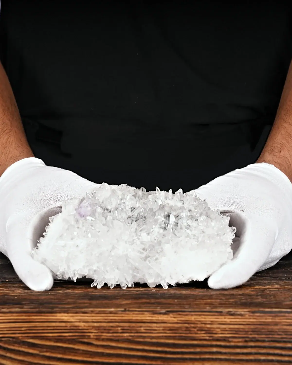 Die Bergkristall- und Amethyst-Nadelstufe in weiss behandschuhten Händen