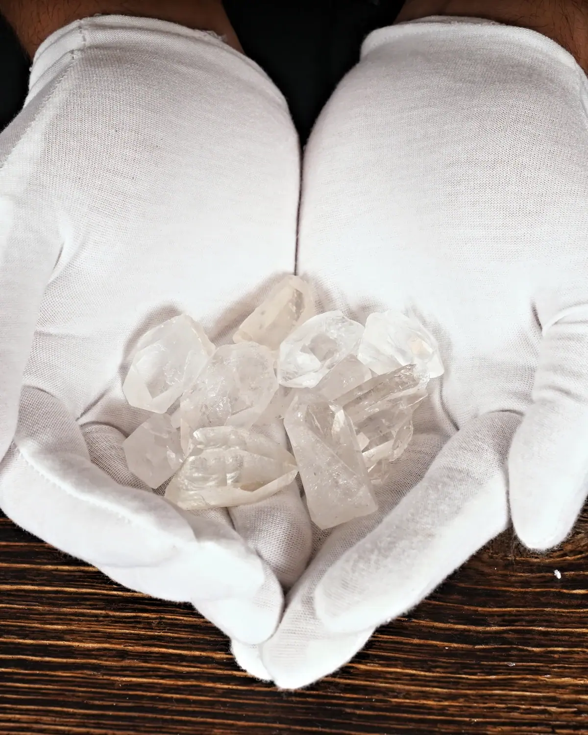 Bergkristall-Rohsteine und Wassersteine in weiss behandschuhten Händen