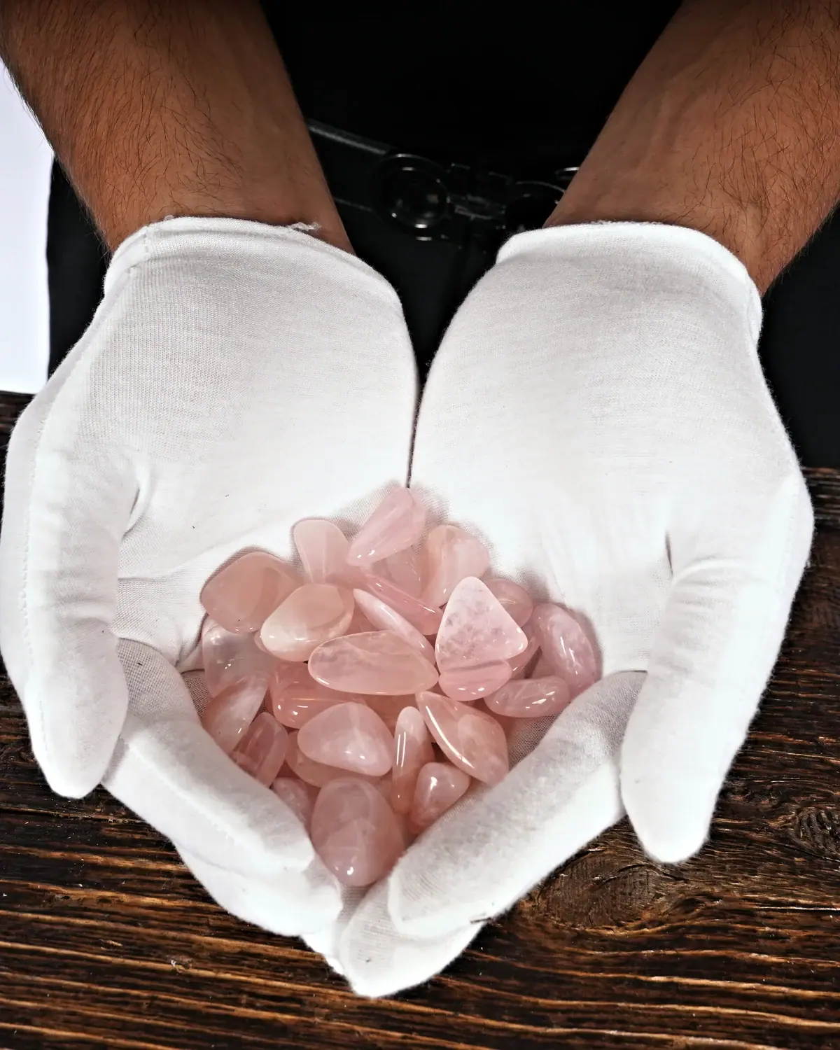 Rosenquarz-Trommelsteine in weiss behandschuhten Händen